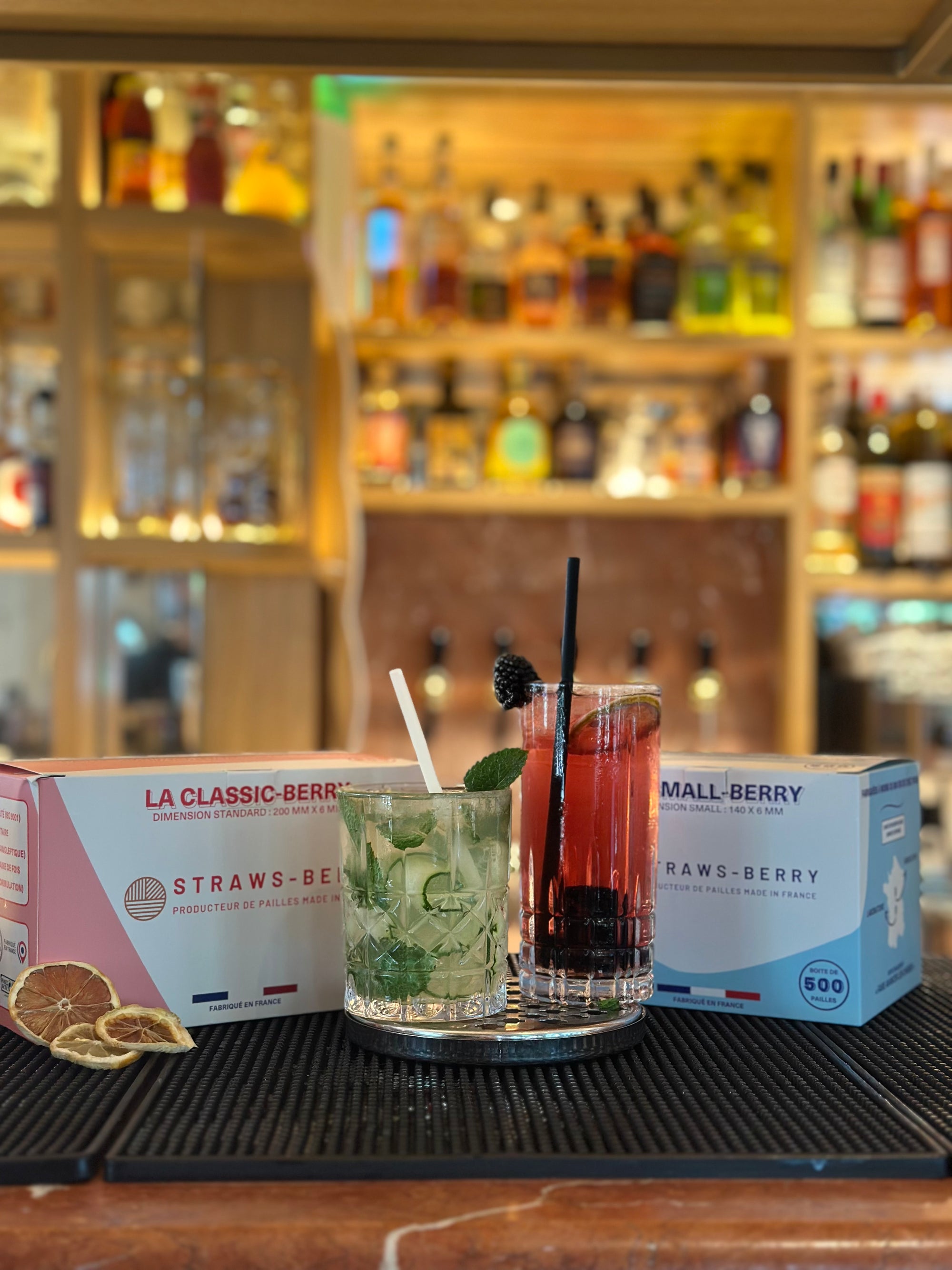 Pailles Classic-Berry noir roche et Small-Berry blanc givré de la marque Straws-Berry dans deux cocktails différentssur un bar professionnel avec les boîtes des deux pailles